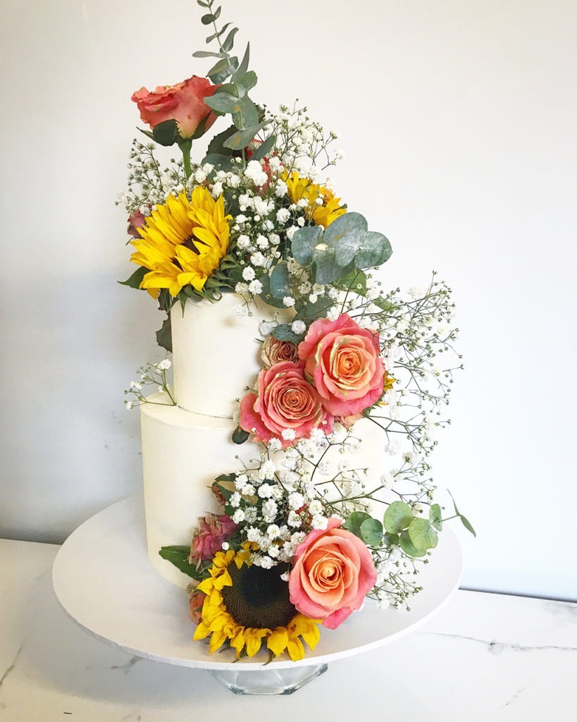 A two tier wedding cake in white with pink roses and sunflowers. A spring wedding