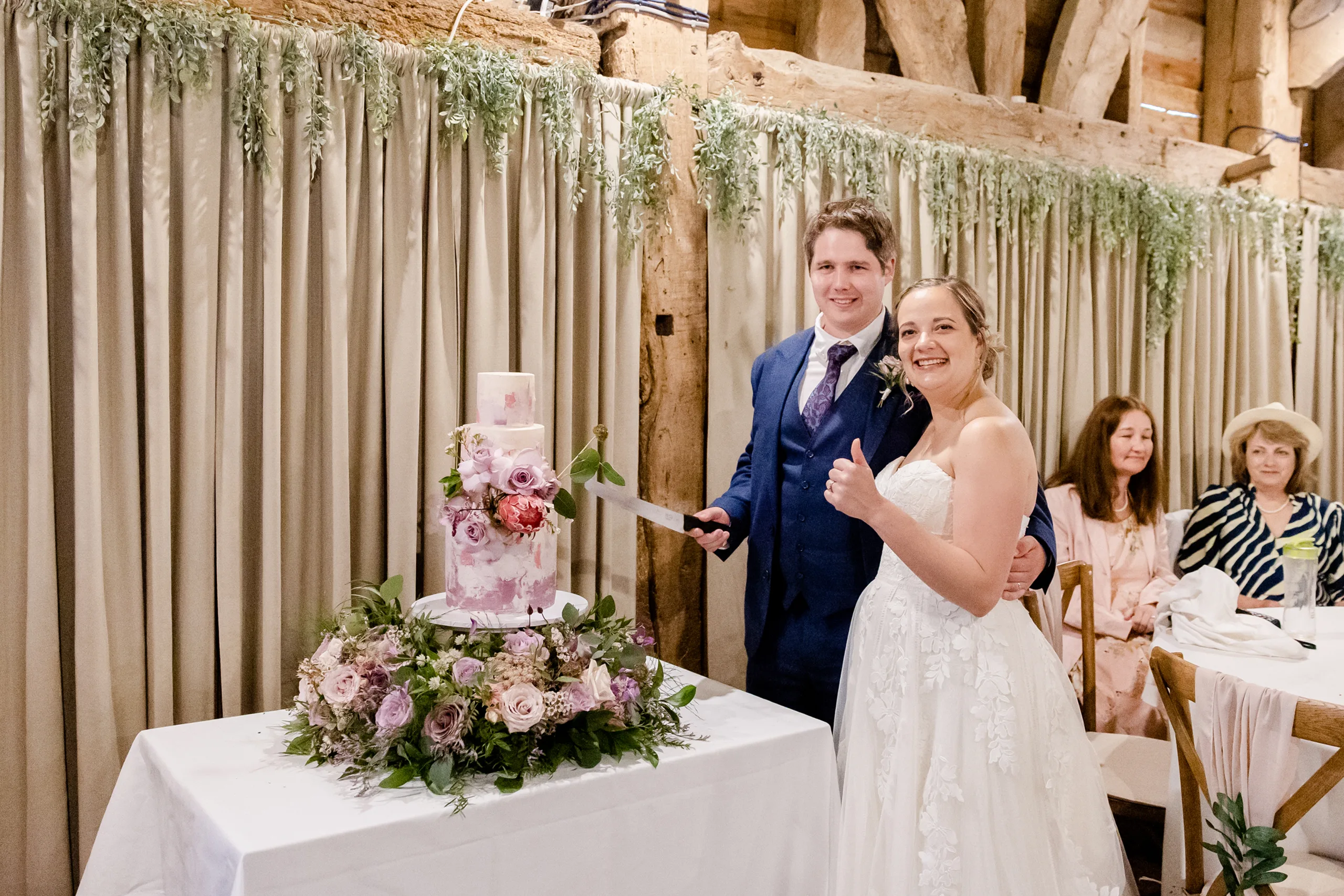 Bride and Groom smiling whilst cutting their three tier mauve wedding cake