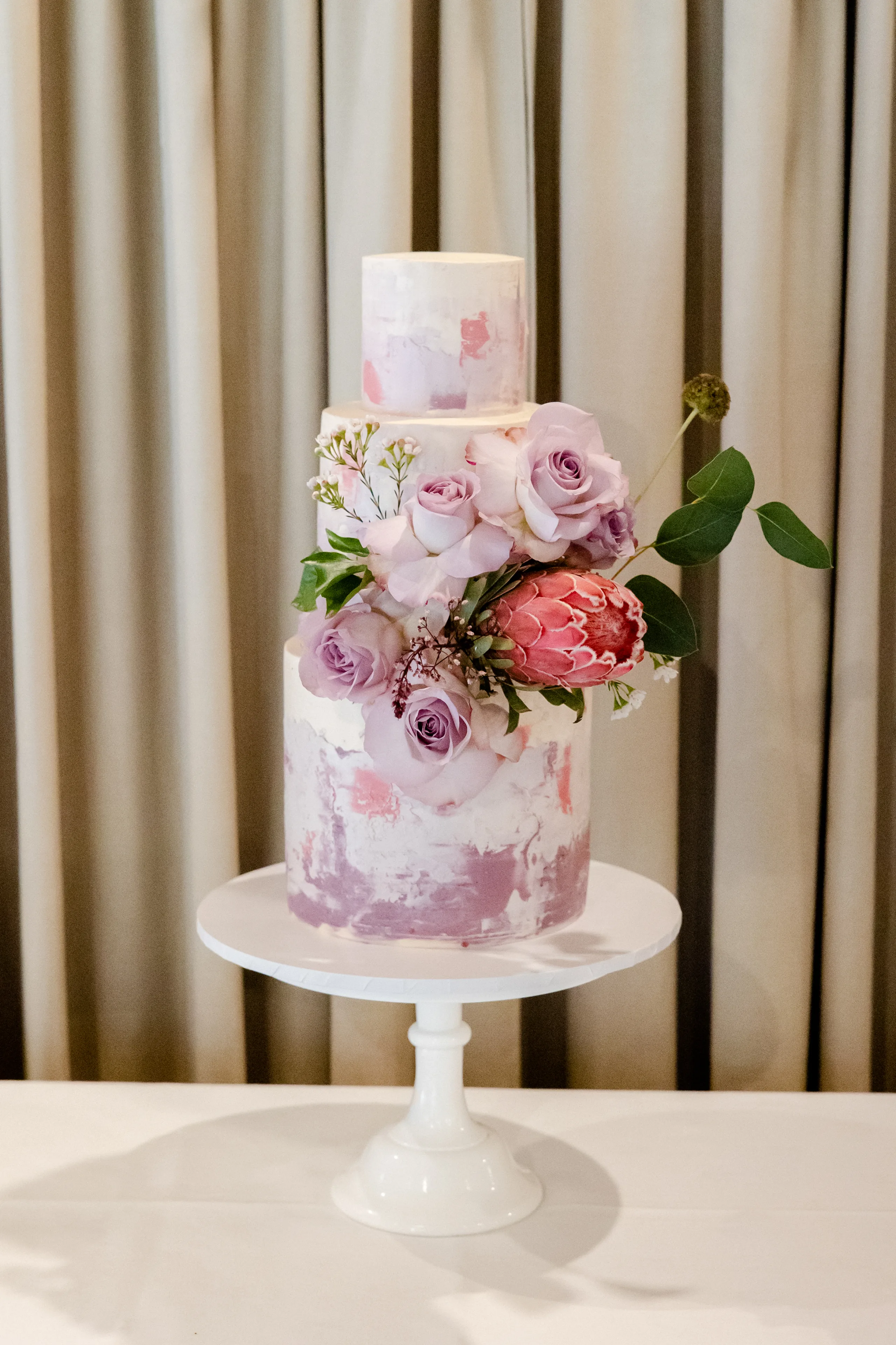 Tree tier wedding cake in Mauve watercolour and floral arrangement with Protea flower and roses