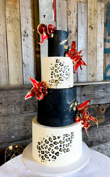 Black and White Leopard Print Wedding Cake with four tiers of cake alternating between black and white. Red fruit petals at off centre placement in a rustic barn backdrop