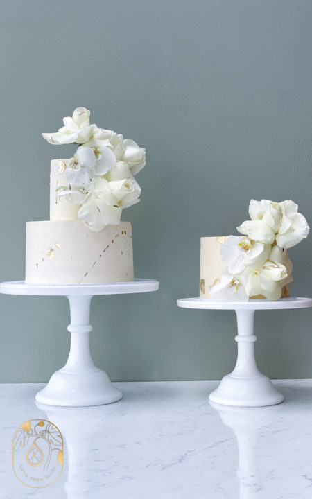 Two matching wedding cakes in white and gold with white roses, orchids and gold