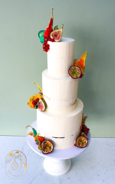 Tree tier wedding cake in semi-naked design with tropical fruits and fruit petals