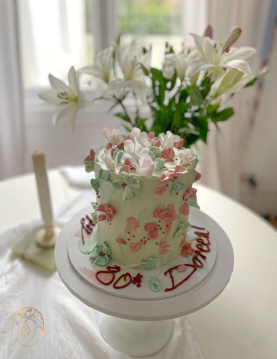 Hand painted celebration cake design. Pastel pink and mint green hand piped buttercream flowers. Message: Happy 80th Birthday Doreen.